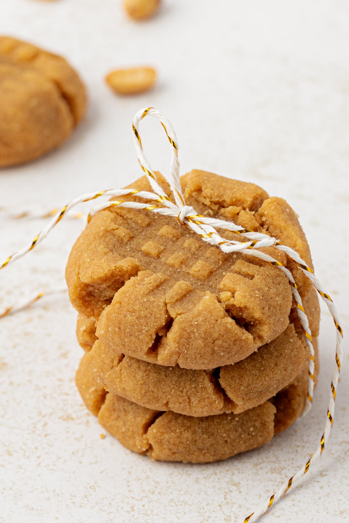 three peanut butter cookies tied in a stack with white and brown string with another cookie and peanuts sprinkled in the background