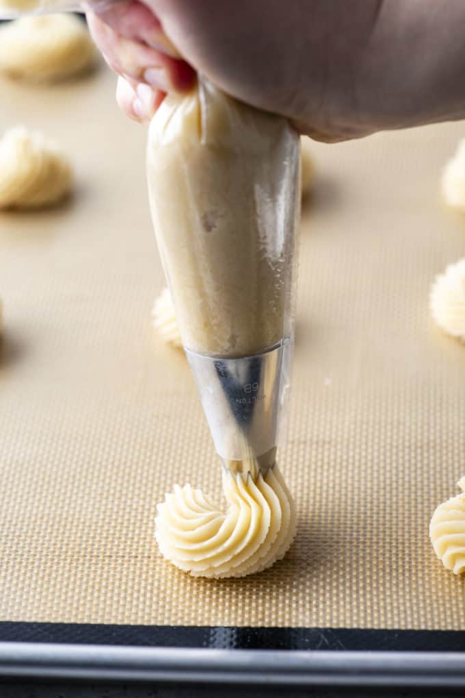 butter cookies being piped onto a cookie sheet lined with a silicone mat