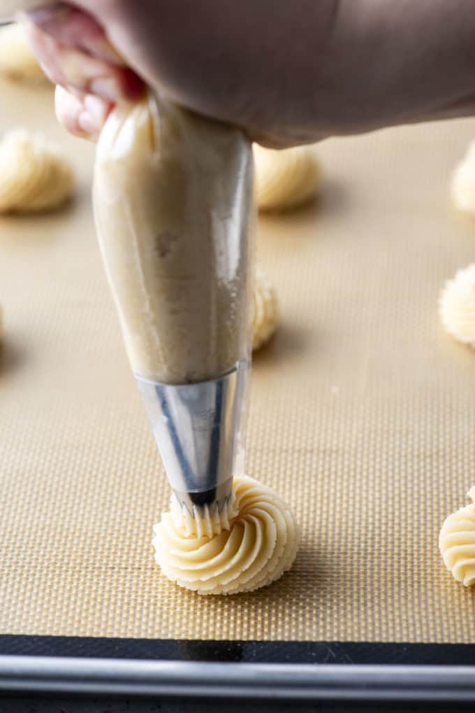butter cookies being piped onto a cookie sheet lined with a silicone mat
