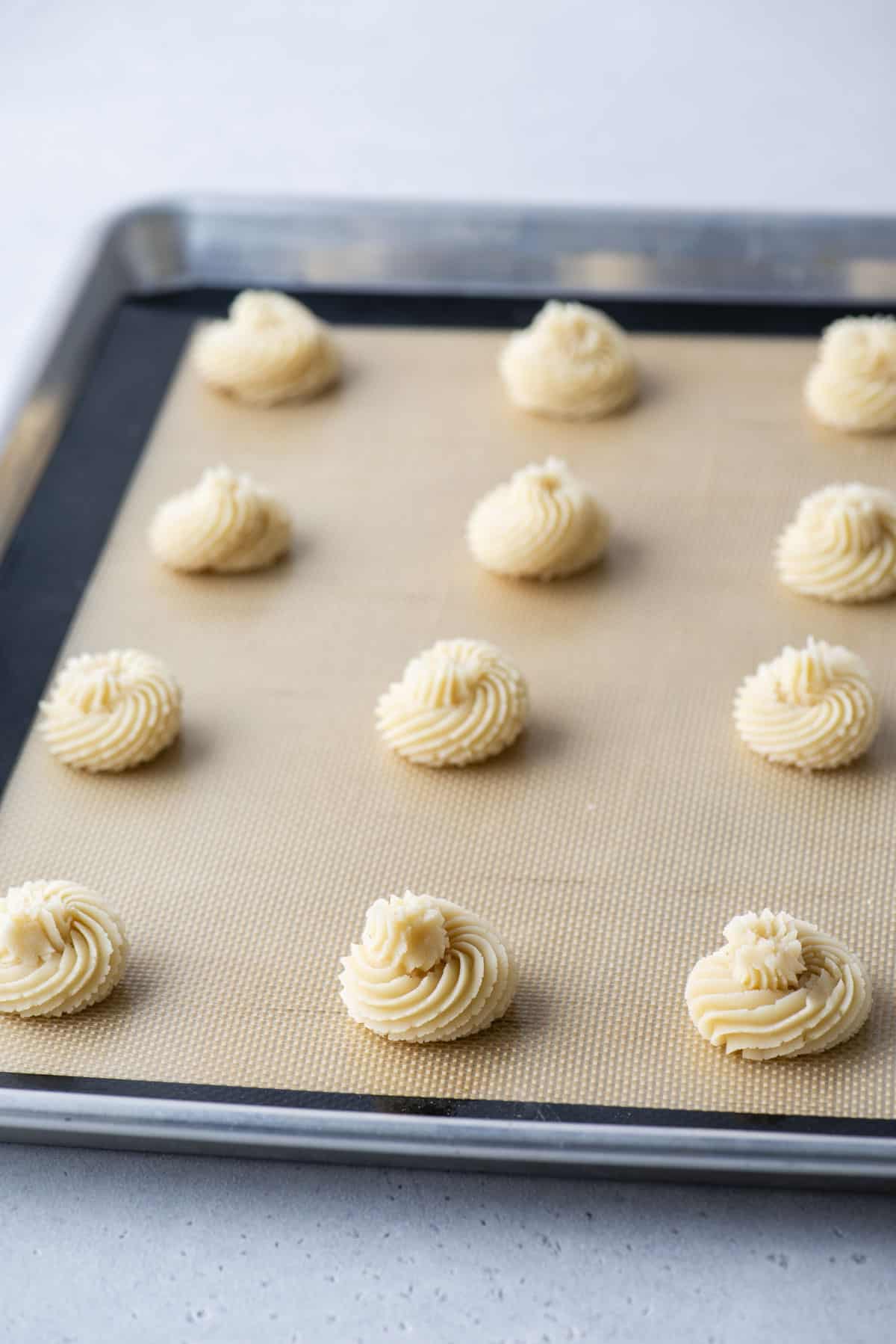butter cookies lined in rows on a cookie sheet covered with a silicone mat