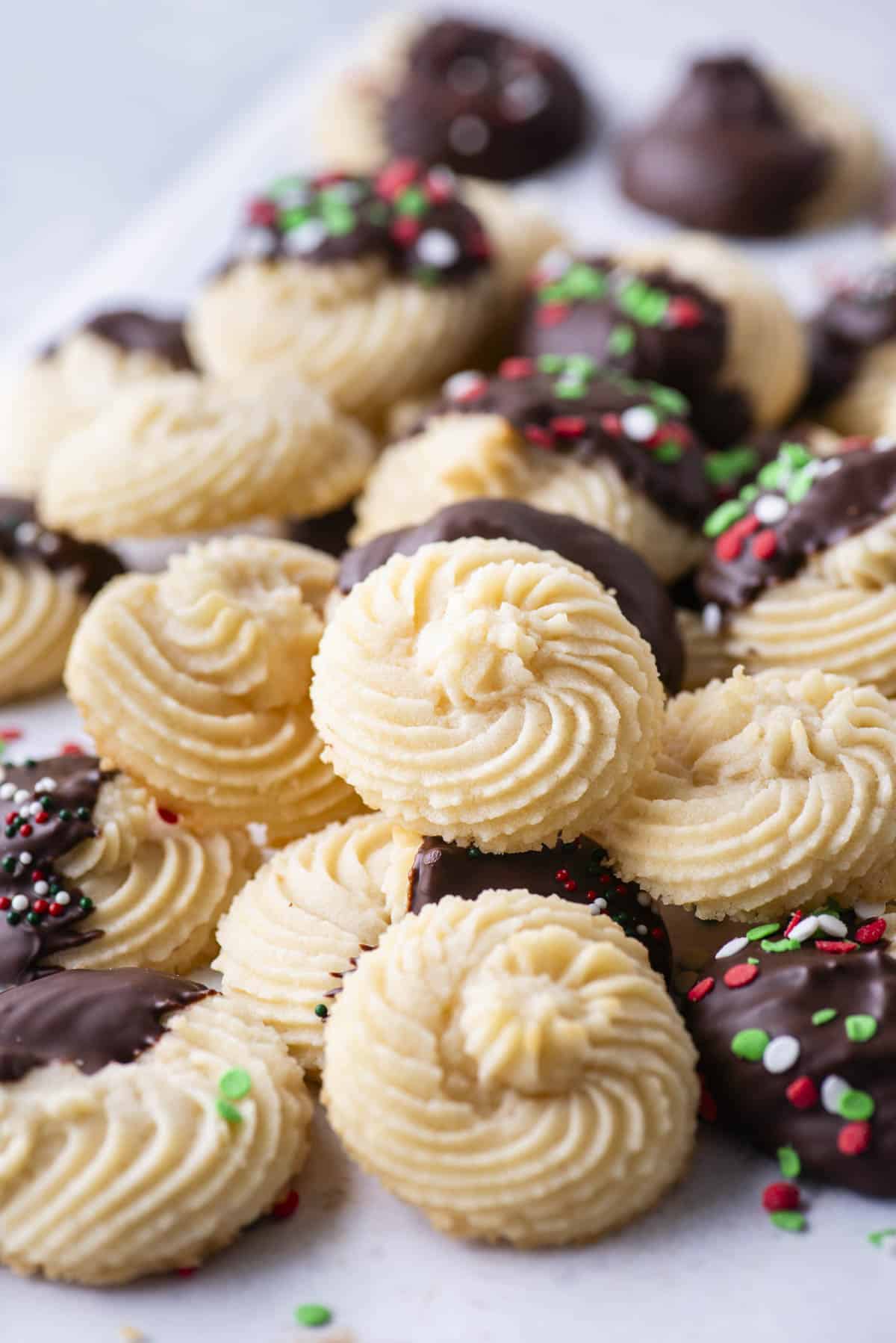 An assortment of butter cookies piled on top of each other, some plain cookies, some dipped in chocolate and some dipped in chocolate with red, green and white sprinkles