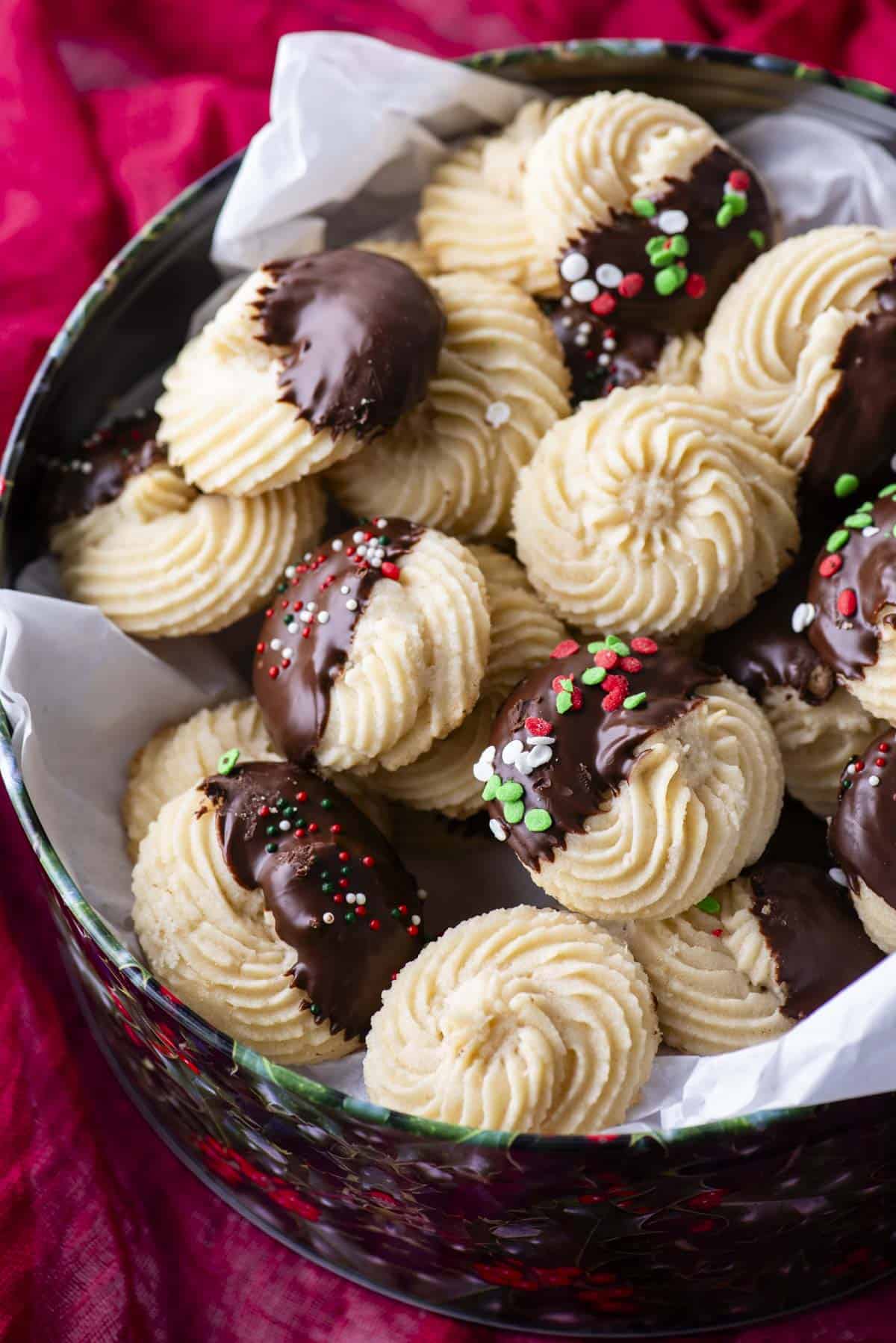 a christmas tin full of butter cookies, some plain and some dipped half in chocolate, some also dipped in red, green and white sprinkles