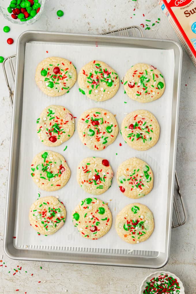 four rows of christmas sprinkle cookies on a baking sheet lined with parchment paper on top of a wire rack