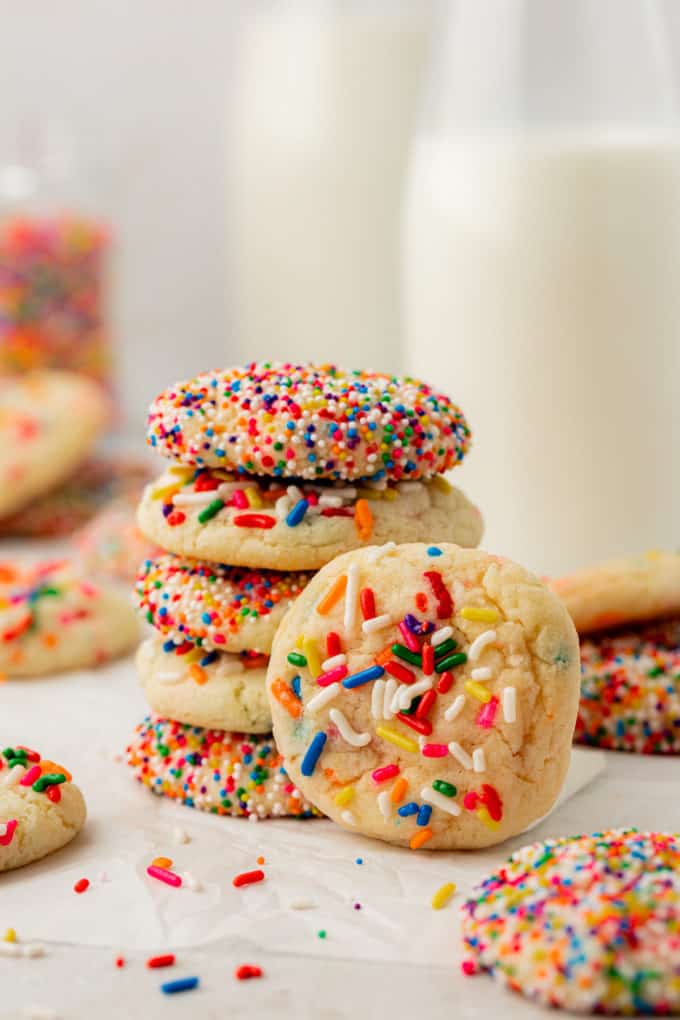 a stack of 5 funfettie cake mix cookies with one more cookie leaning vertically on the stack and more funfetti cookies all spread around