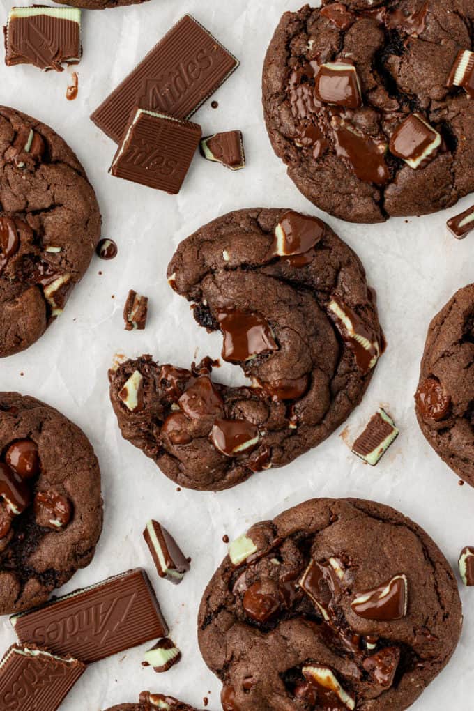 andes mint cookies on white paper with gooey melted chocolate in them, the middle cookie partially pulled apart and bits of andes mints sprinkled throughout