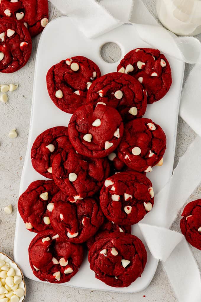 red velvet cake mix cookies on a white board surrounded by sprinkles of white chocolate chips and more cookies