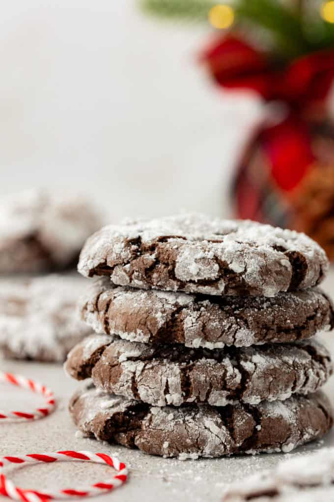 4 chocolate crinkle cake mix cookies in a stack with powdered sugar sprinkled around, a white and red string beside the stack and more cookies in the background