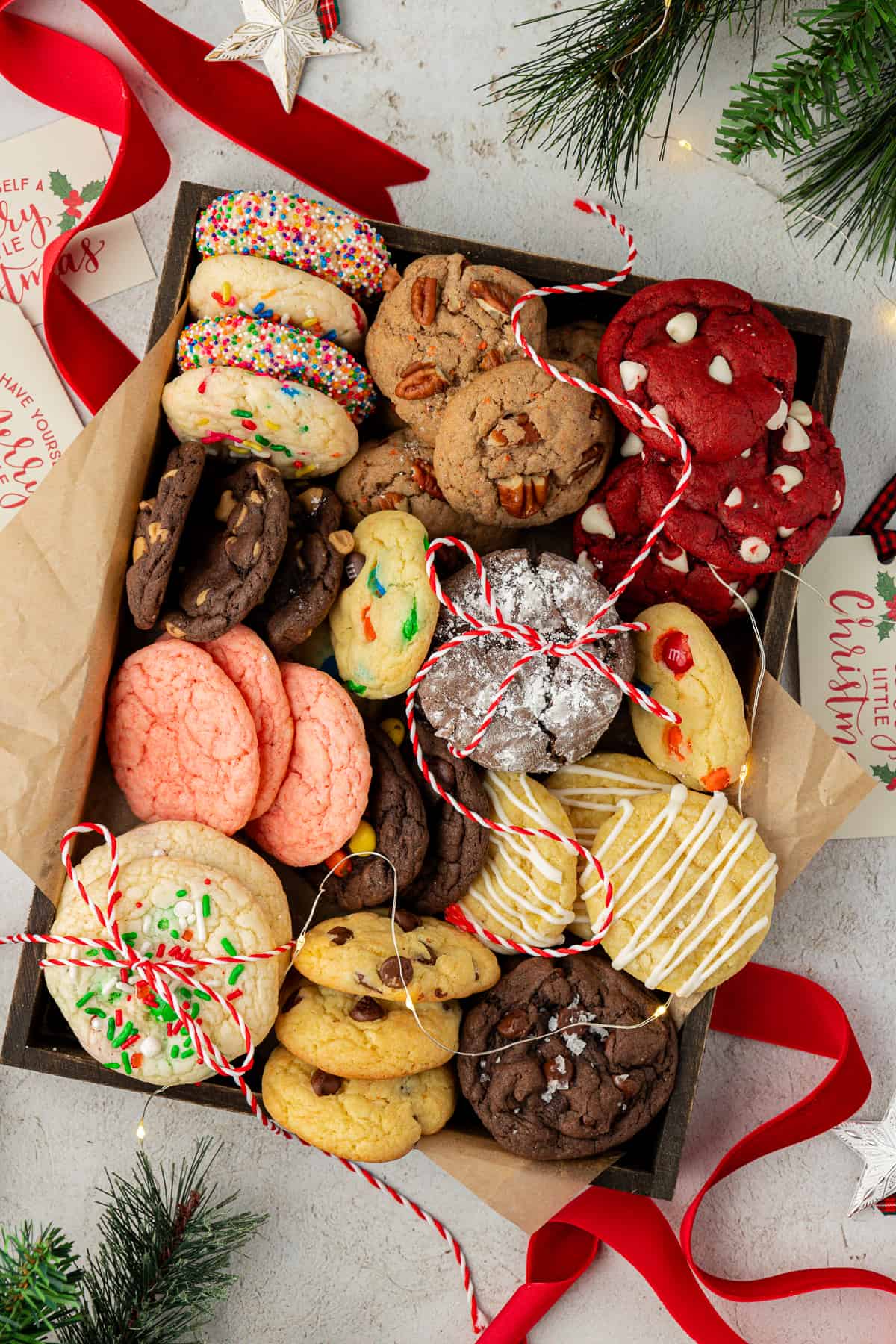 a box full of assorted flavors of cake mix cookies with red ribbon under the box, red and white string on top and pine stems around the box