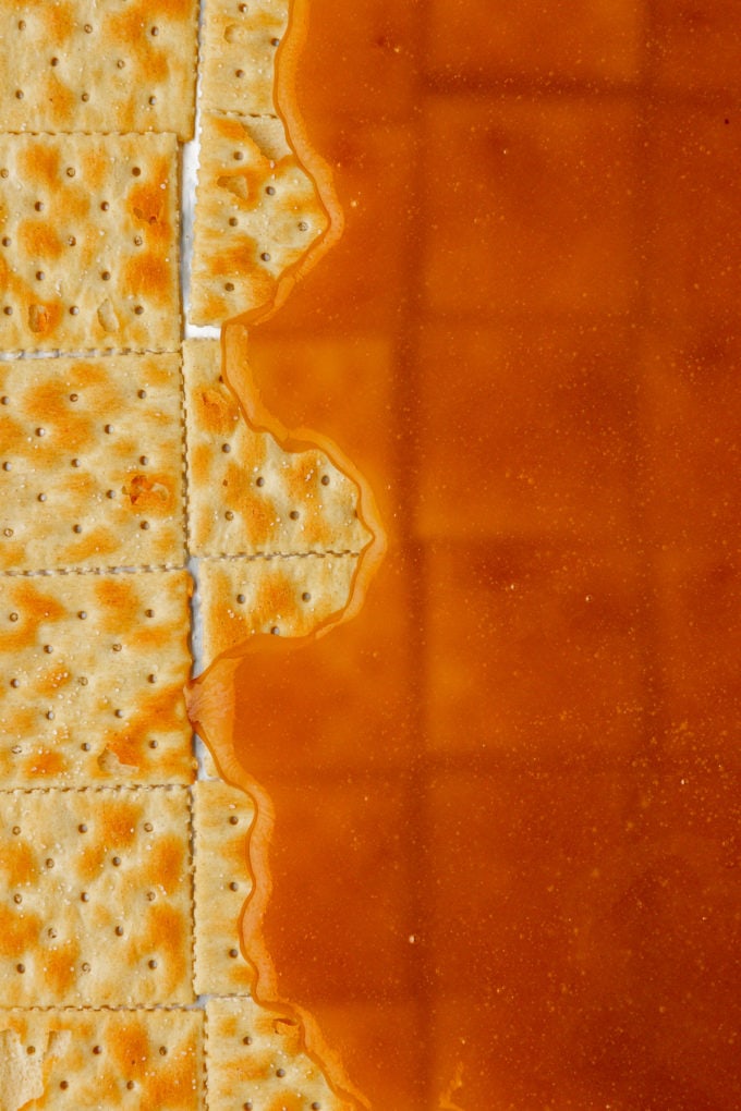 a brown sugar and butter mixture partially poured over a single layer of saltine crackers, with some crackers on the left that haven't been covered yet