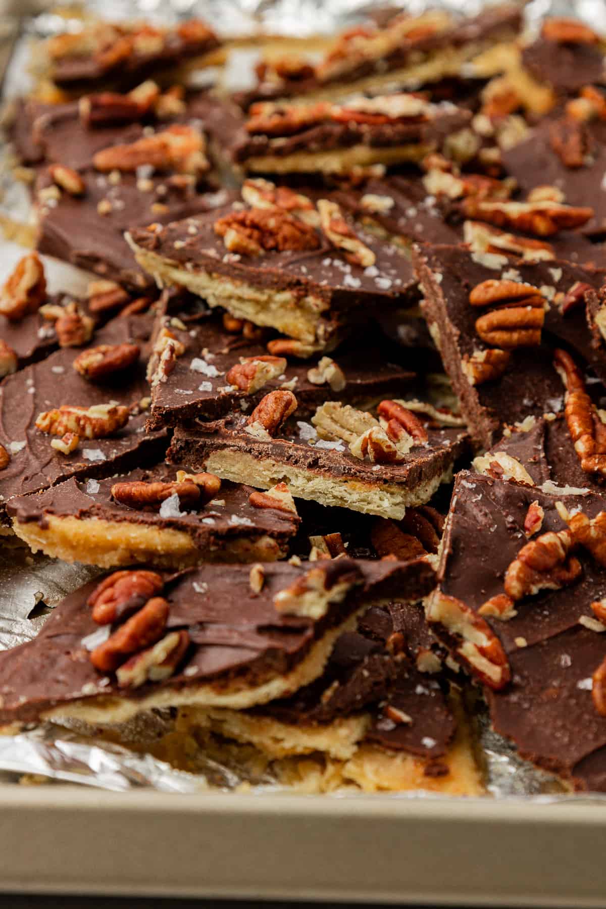 christmas crack candy with pecans and sea salt on top on top of a sheet pan lined with aluminum foil