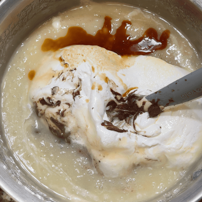 ingredients for fantasy fudge with marshmallow creme on top being mixed in a pot with a rubber spatula