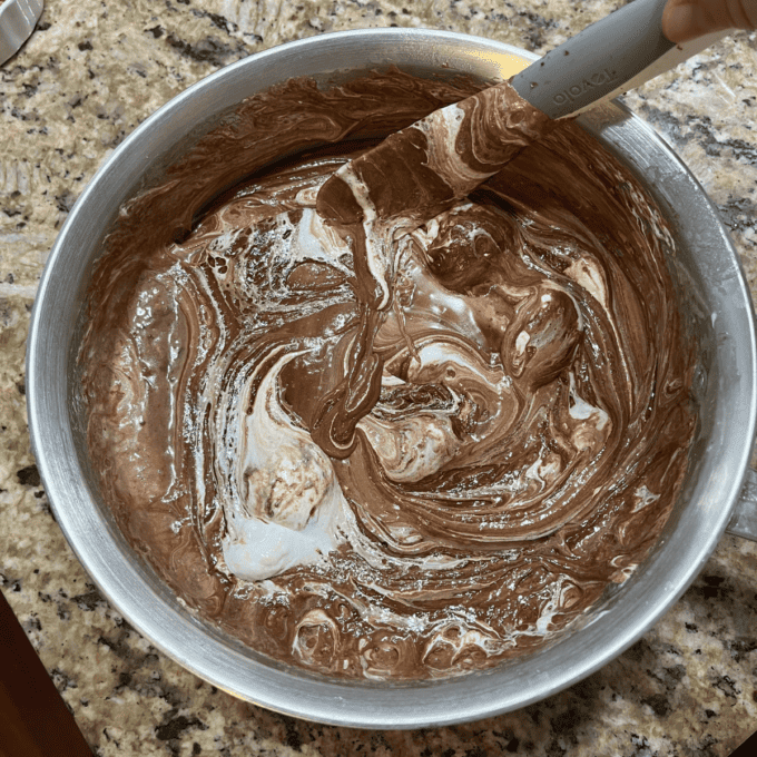 ingredients for fantasy fudge mixed in a pot with a rubber spatula sitting on a granite countertop