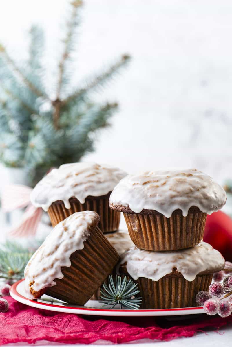gingerbread muffins with vanilla glaze arranged on white plate with red sugared berries and evergreen branches