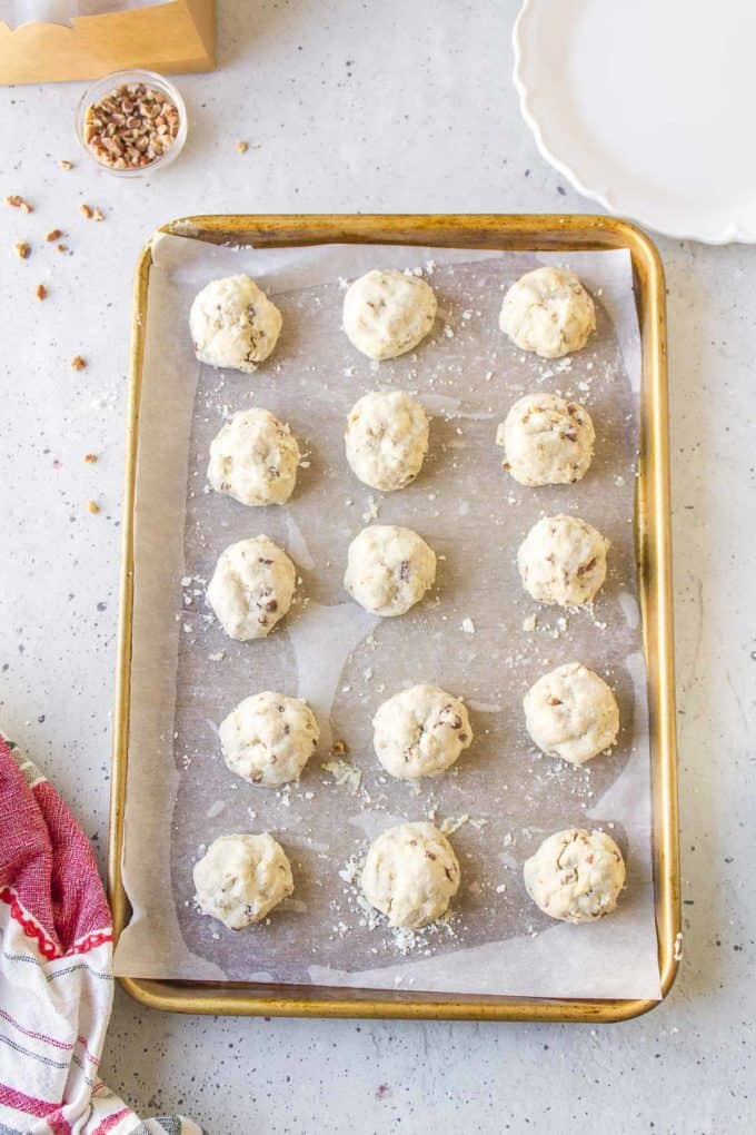 rows of freshly baked mexican wedding cookies on a sheet pan that has been lined with parchment paper