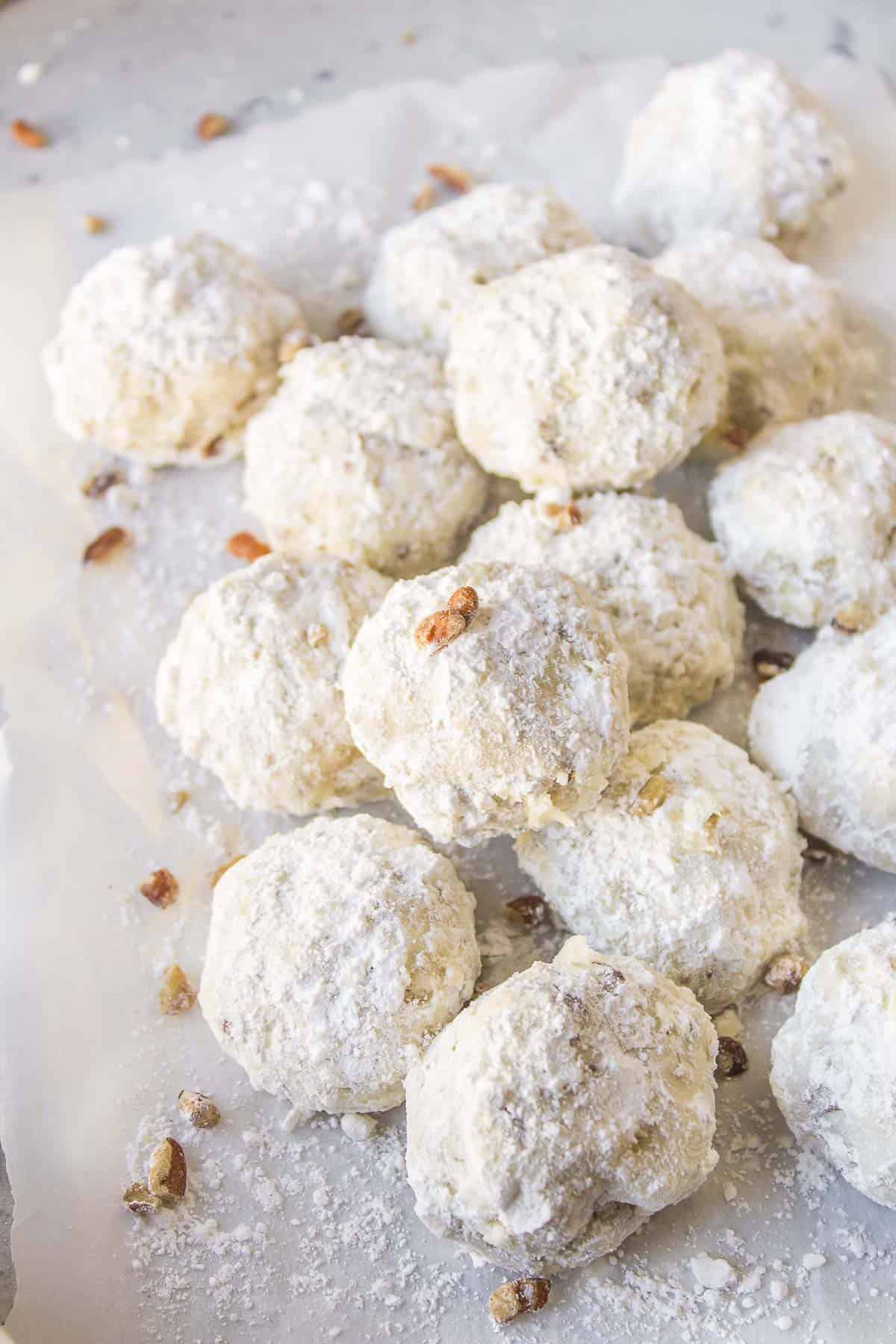 a pile of mexican wedding cookies on white parchment paper with some chopped pecans sprinkled on them