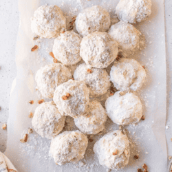 a pile of mexican wedding cookies on white parchment paper on a white counter