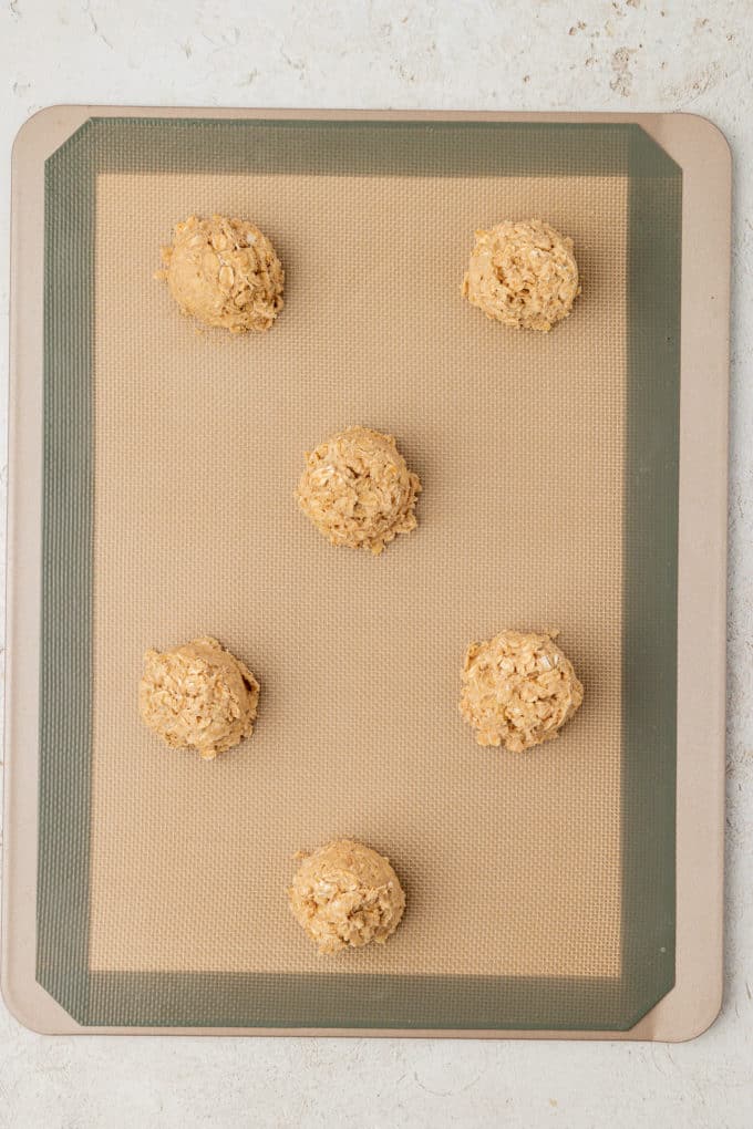 oatmeal cookie dough balls on a silicone baking mat on a baking sheet