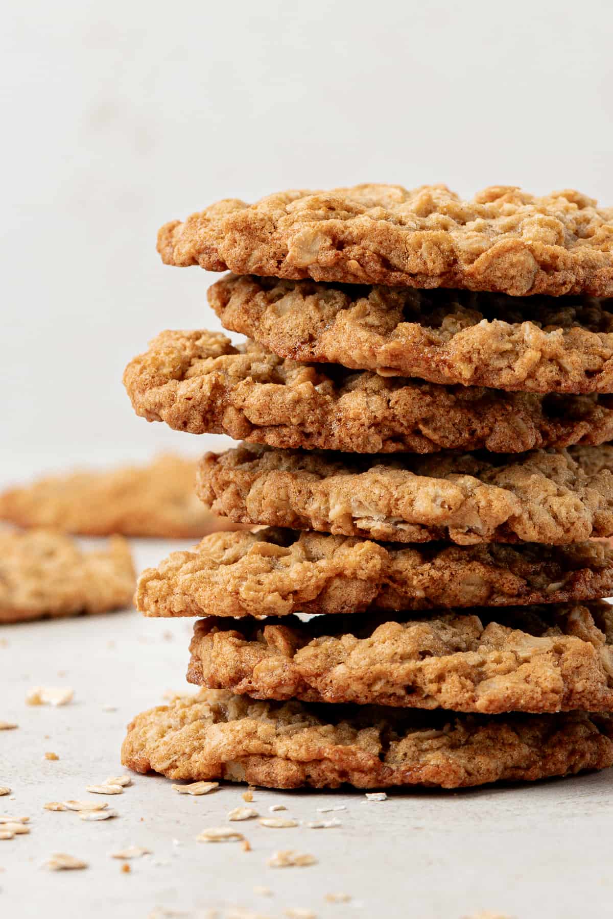 a stack of oatmeal cookies with more cookies and oats sprinkled in the background