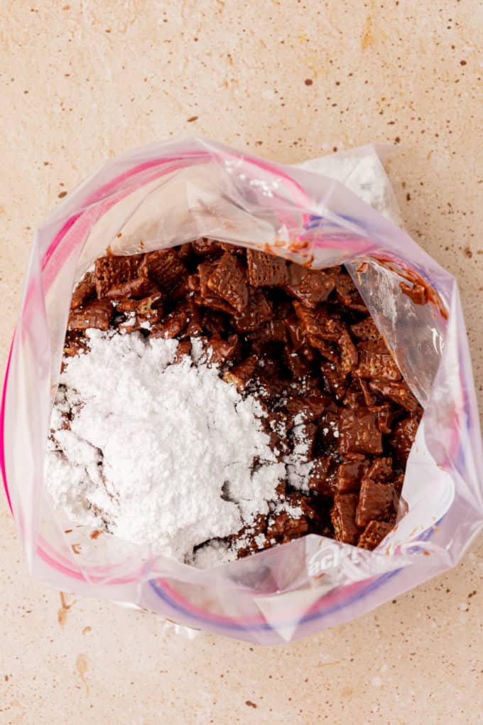 chex cereal coated in chocolate in a large ziploc bag with a pile of powdered sugar on top