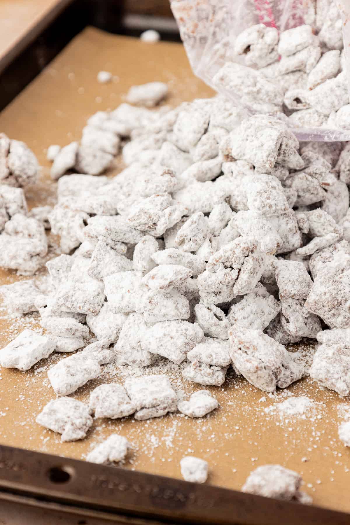 A pile of puppy chow spilled out of a ziploc bag onto a sheet pan lined with parchment paper