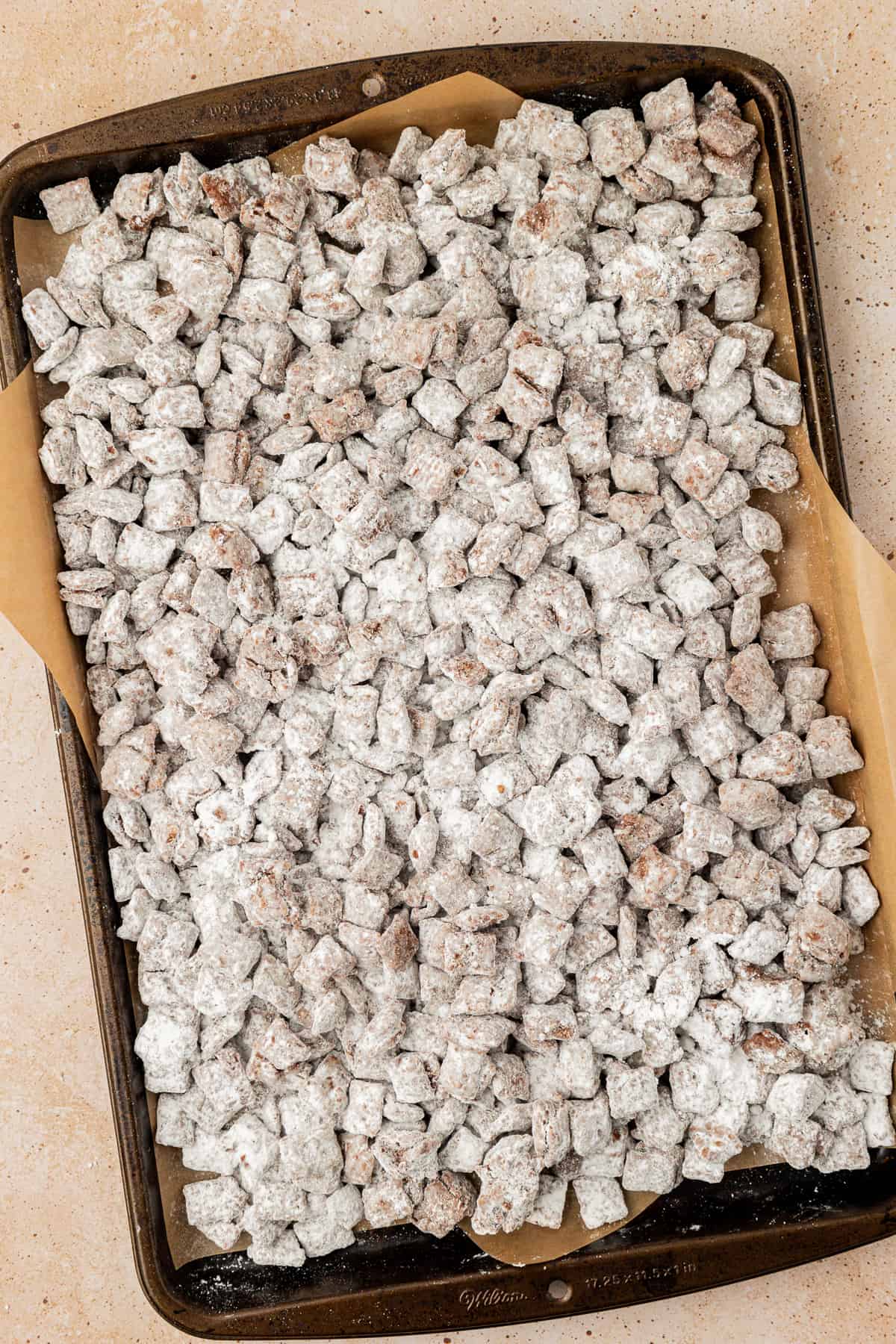 a sheet pan lined with parchment paper full of puppy chow/muddy buddies