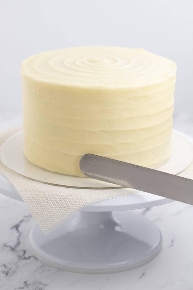 a red velvet cake being frosted with cream cheese frosting on top of a white cake stand