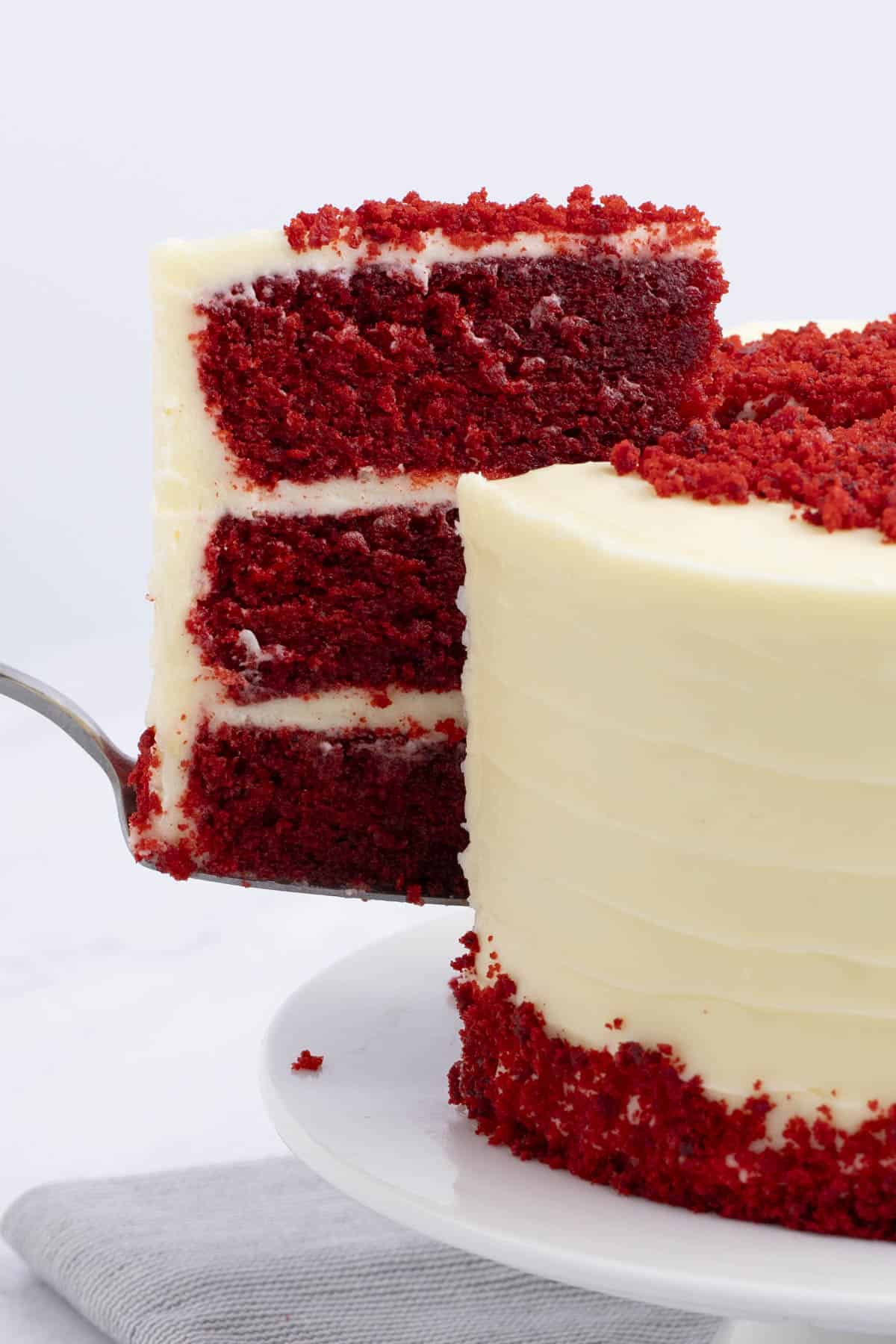 the side view of a slice of red velvet cake being lifted out of the whole cake with a serving knife