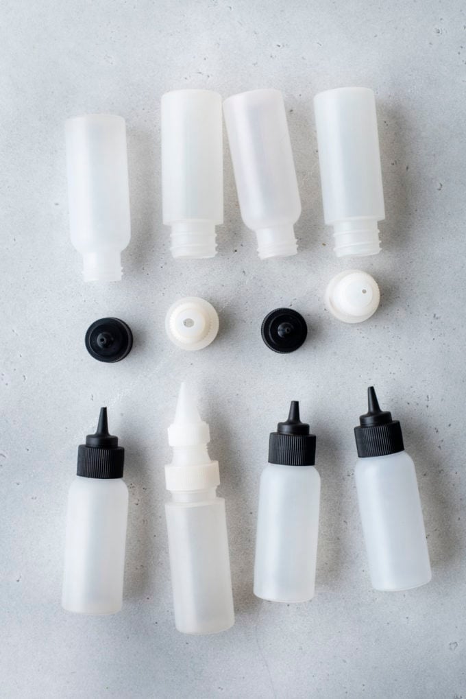 squeeze bottles with lids, some white lids and some black lids, laying on their sides on a counter top