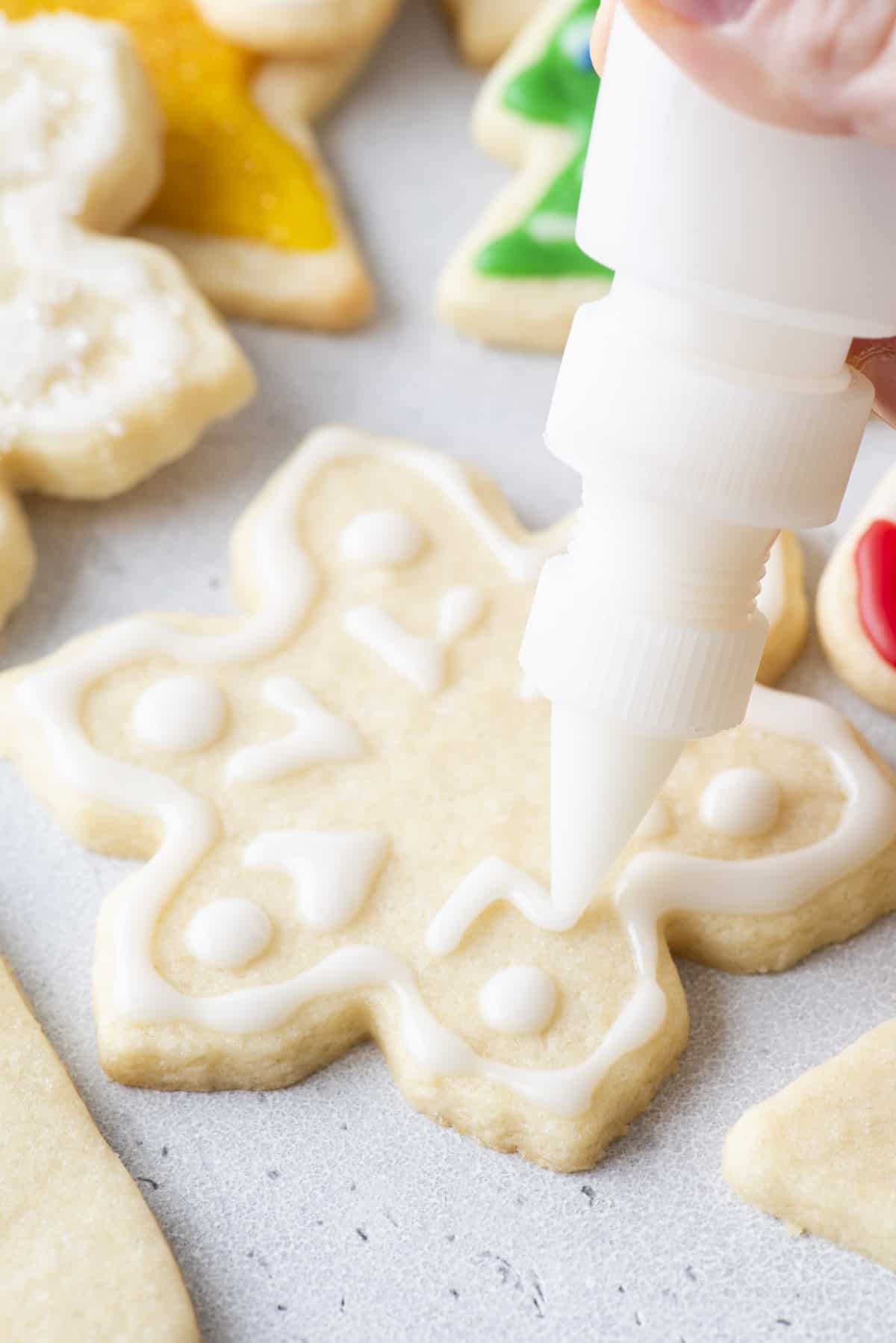 white royal icing being piped onto a snowflake shaped cookie with a squeeze bottle