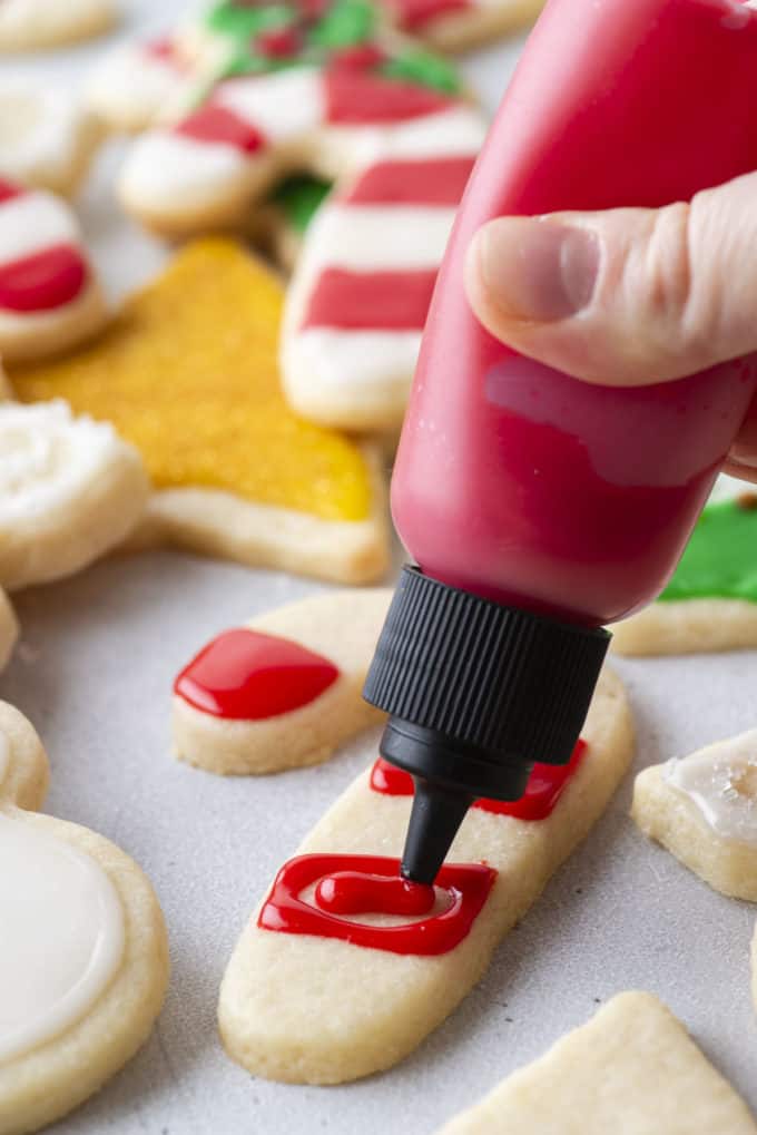 red royal icing being piped onto a candy cane shaped cookie using a squeeze bottle