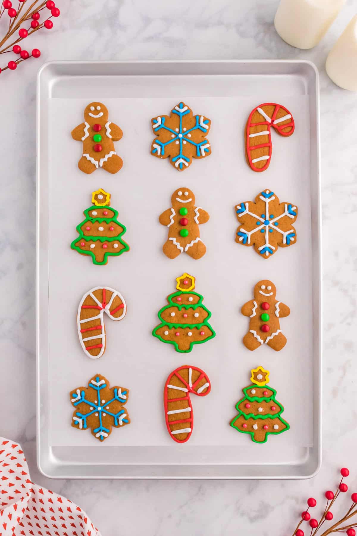 an assortment of gingerbread cookies decorated with royal icing lined in rows on a cookie sheet lined with parchment paper