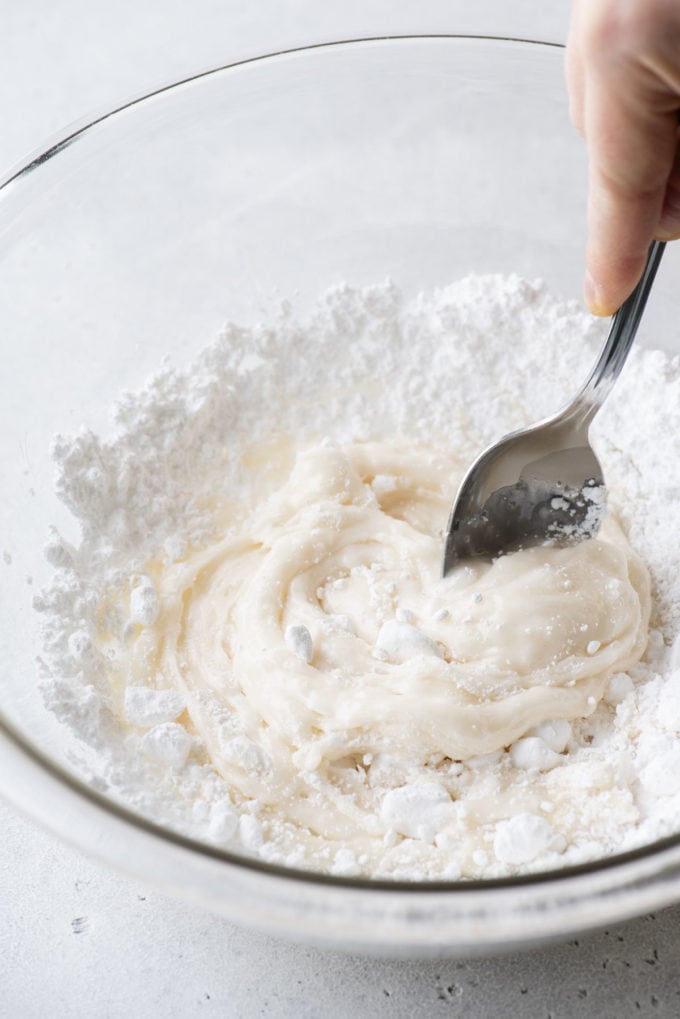 royal icing ingredients being mixed together with a spoon in a clear glass bowl
