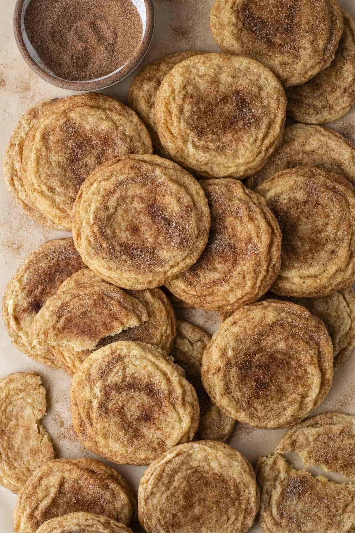close up on a pile of snickerdoodle cookies with a bowl of cinnamon sugar 