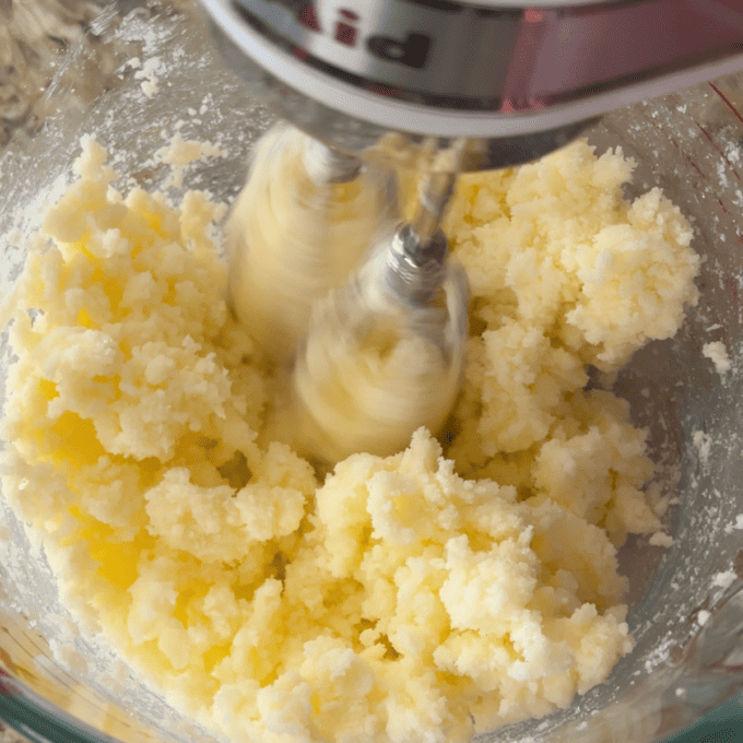 butter and sugar being mixed together with an electric mixer in a glass mixing bowl