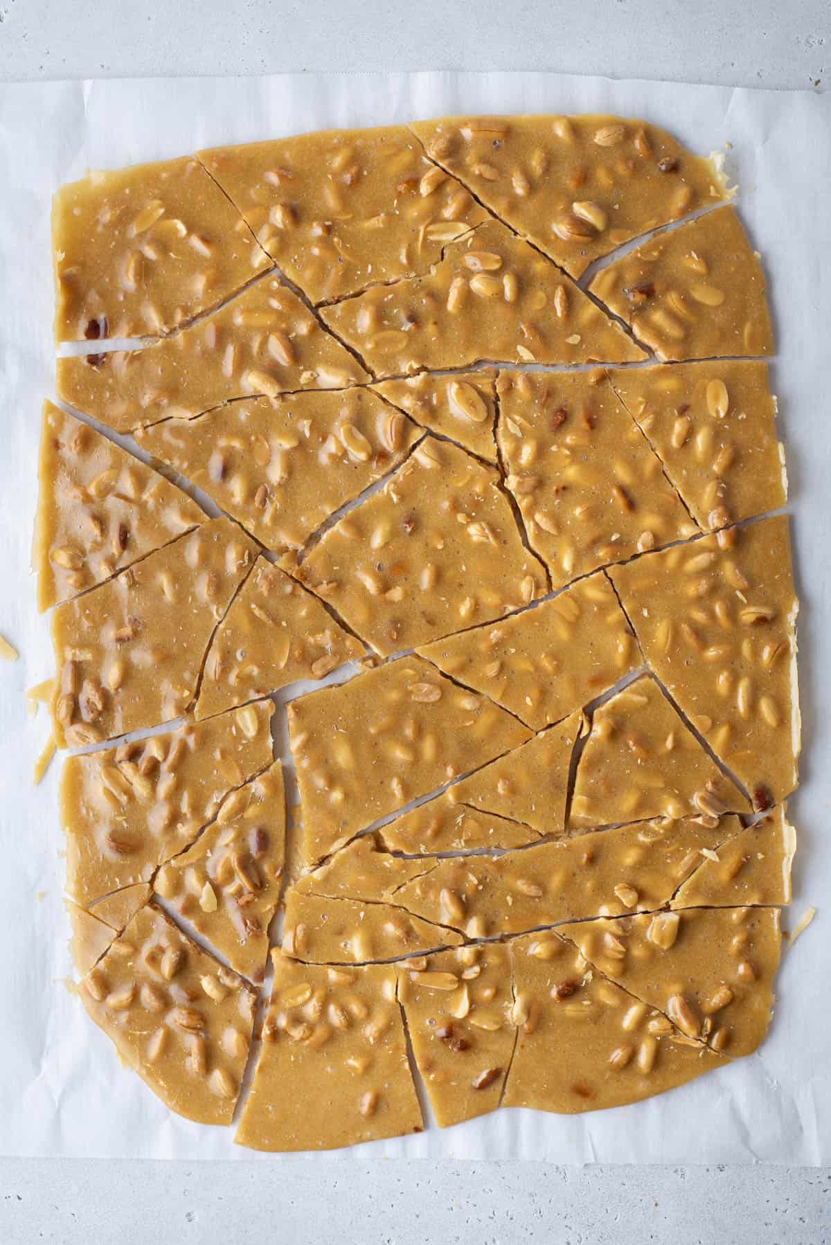 peanut brittle broken into pieces on a baking sheet lined with parchment paper