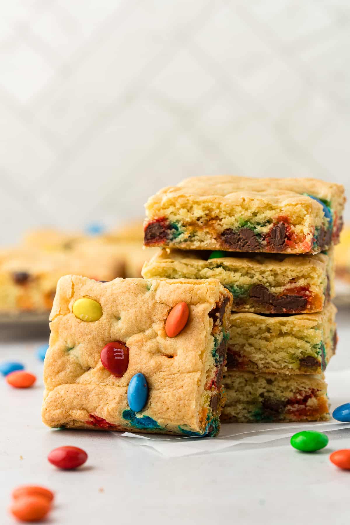 a stack of cake bars with another square cake bar leaning up against the stack and more bars in the background with m&ms sprinkled around