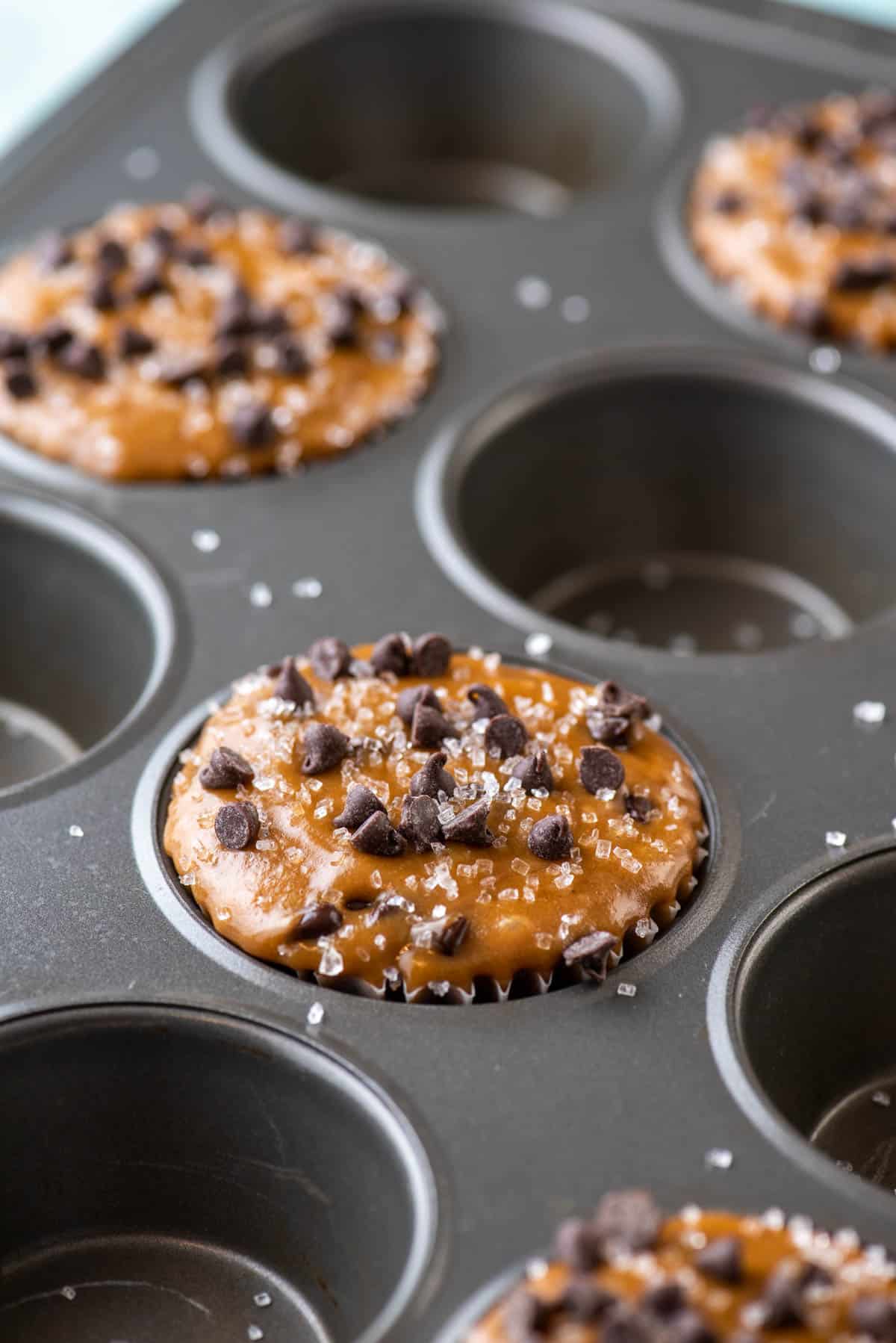 cappuccino chip muffin batter filling every other hole of a muffin pan, topped with mini chocolate chips and sprinkled with sanding sugar