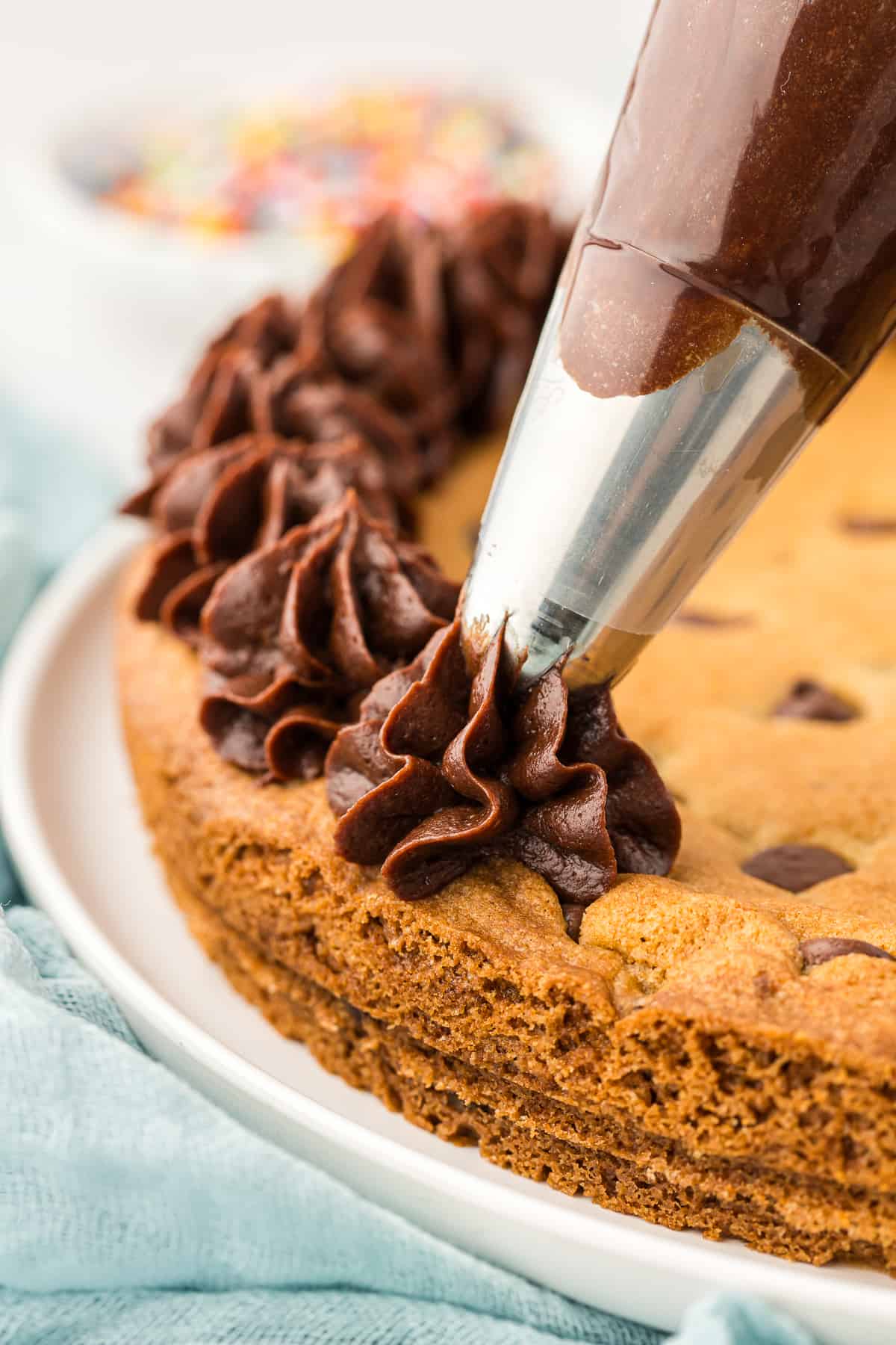 cookie cake being decorated with chocolate frosting from a piping bag