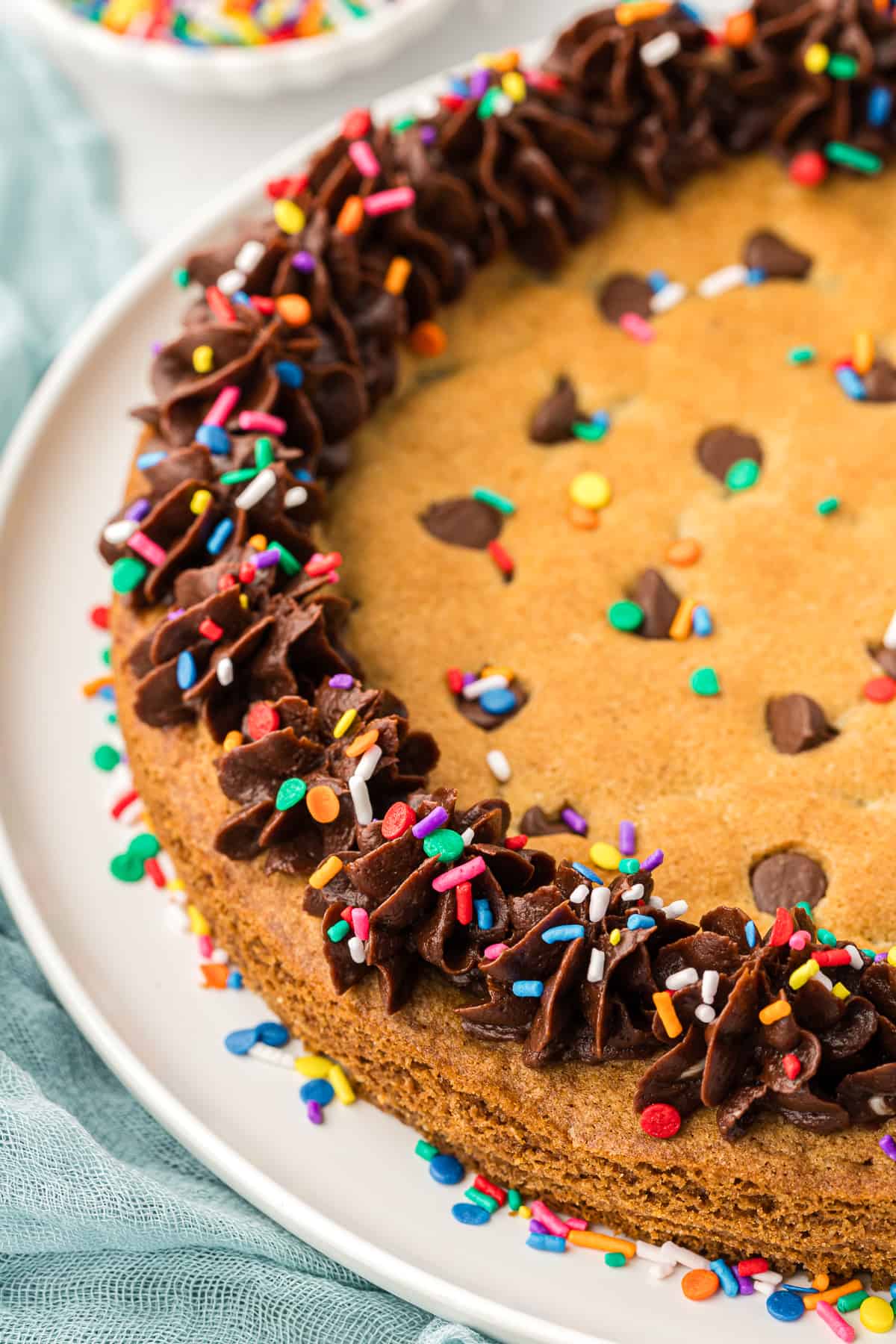 a round cookie cake on a white plate topped with chocolate frosting and colored sprinkles