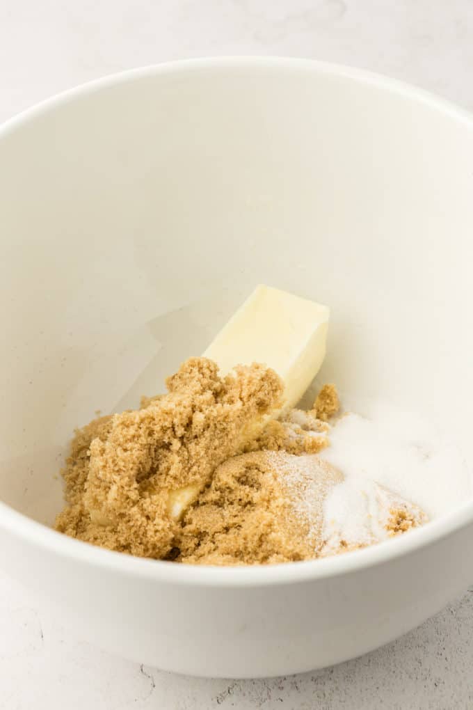 a stick of butter, brown sugar and granulated sugar in a white bowl