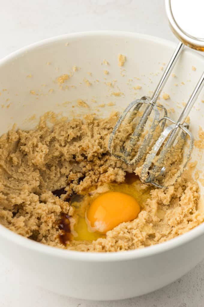 wet ingredients for cookie cake in a white bowl with an electric mixer leaning in the side of the bowl