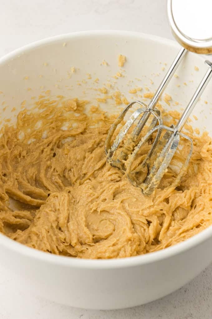 wet ingredients for cookie cake in a white bowl with an electric mixer leaning in the side of the bowl