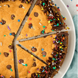 a sliced round cookie cake decorated with chocolate frosting and colored sprinkles on a white plate
