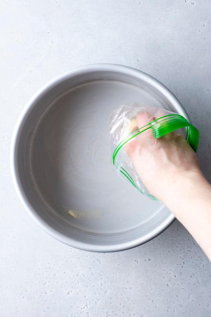 a hand inside a small ziploc bag holding a piece of butter and rubbing it inside a round cake pan