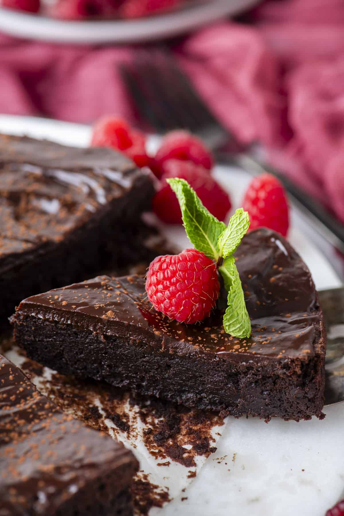 a slice of flourless chocolate cake being lifted away from the rest of the cake, topped with a fresh raspberry and mint leaves