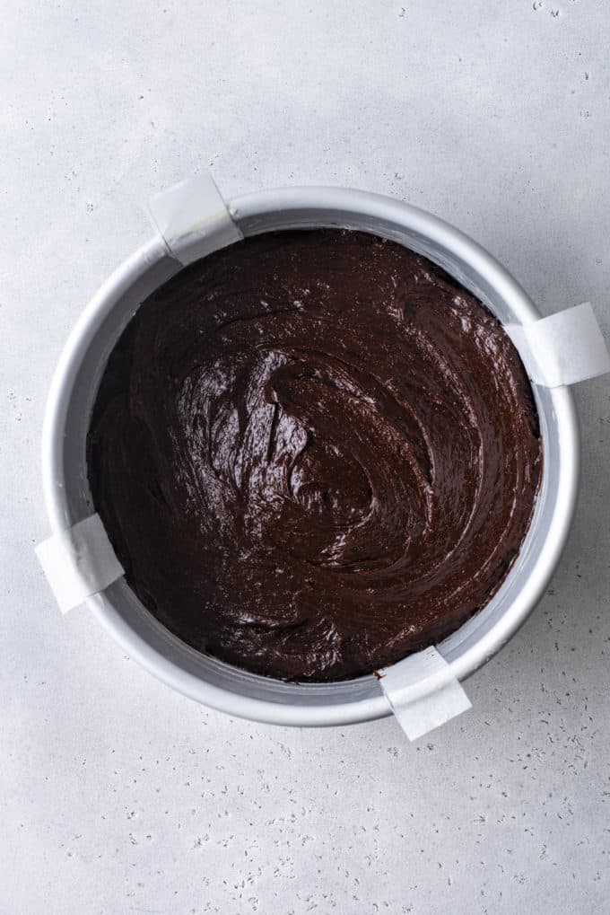 flourless chocolate cake batter in a round cake pan with four parchment paper handles sticking out the sides