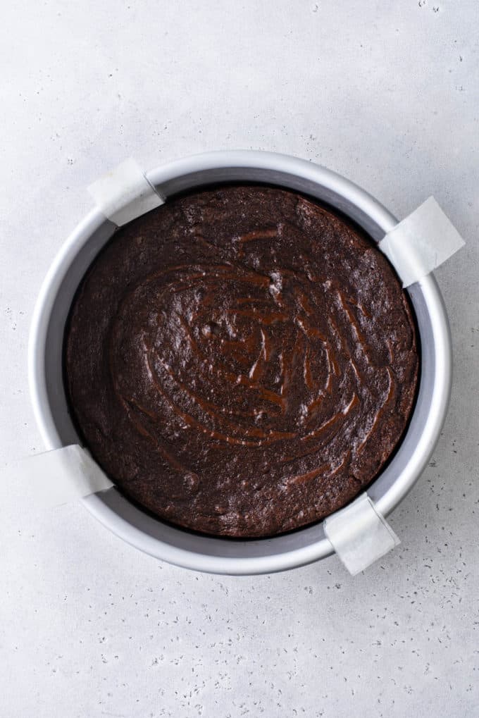 freshly baked flourless chocolate cake in a round cake pan with four parchment paper handles sticking out the sides