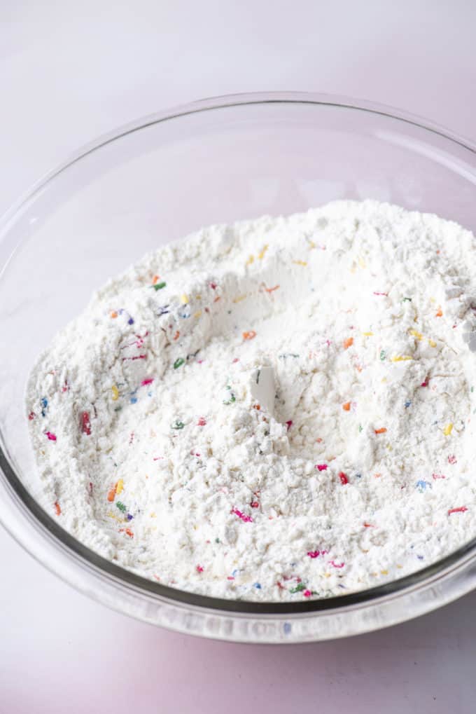 dry ingredients for funfetti cake in a clear glass bowl on a pink surface