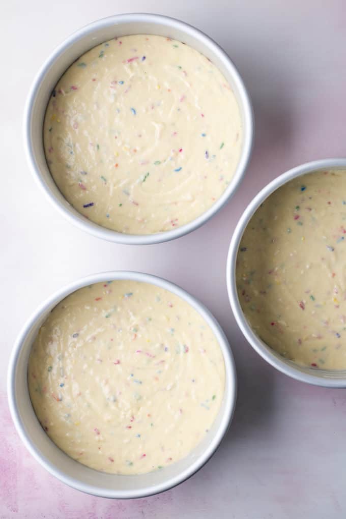 three round cake pans filled with funfetti cake batter