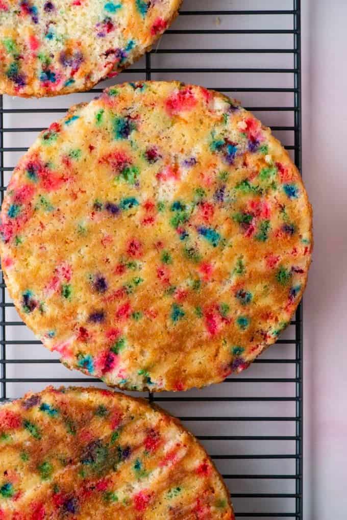 three round funfetti cakes on a wire cooling rack